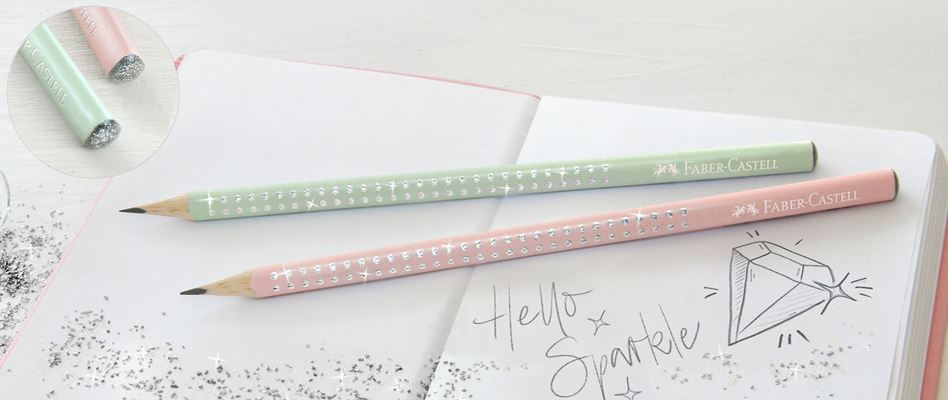 Two pastel green and pastel pink Sparkle graphite pencils with sparkling dots lying on a notebook in which "Hello Sparkle" is written.